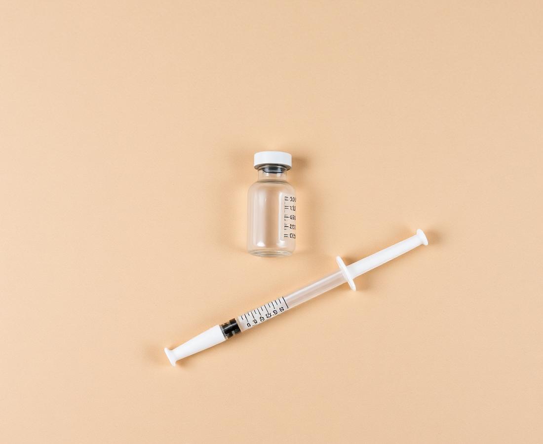 A glass vial beside a syringe on a beige surface
